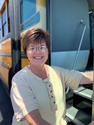 Becky has short brown hair and wears glasses; she has a light yellow shirt with buttons