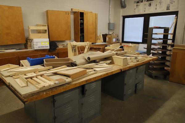 A long table is covered by spare/scrap pieces of wood. They look like they're in good condition, so perhaps these objects are part of an ongoing project.