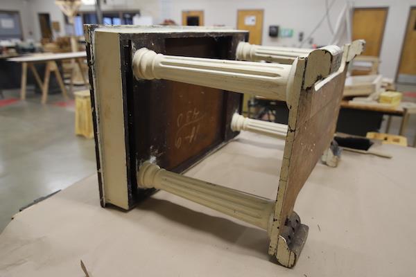 White wooden table laying sideways on another table. It looks like it's being worked on.