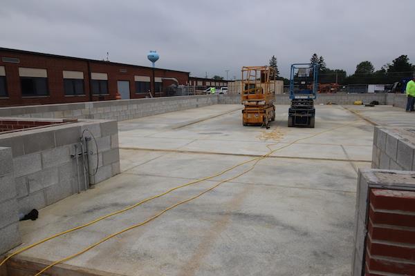 Another view of the greenhouse's (incomplete) entryway. It shows the concrete foundation and two machines standing atop it. You can see the brickwork on top of the foundation.