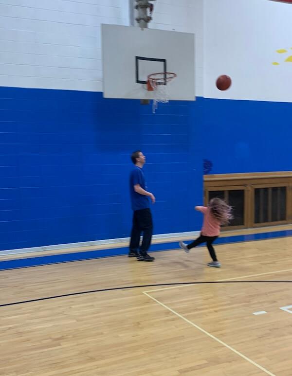 A little girl throws a basketball to the goal.. the ball is quite close to making a basket!